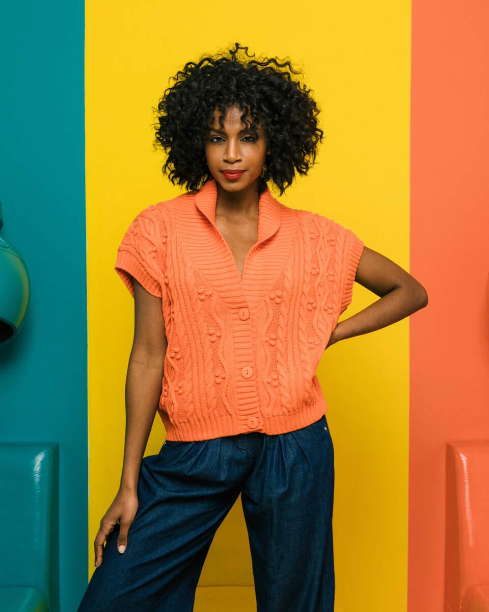 Πλεκτή αμάνικη πορτοκαλί ζακέτα με V λαιμόκοψη, άνοιγμα στην πλάτη και μπροστά κουμπιά. Εμφάνιση από μπροστά