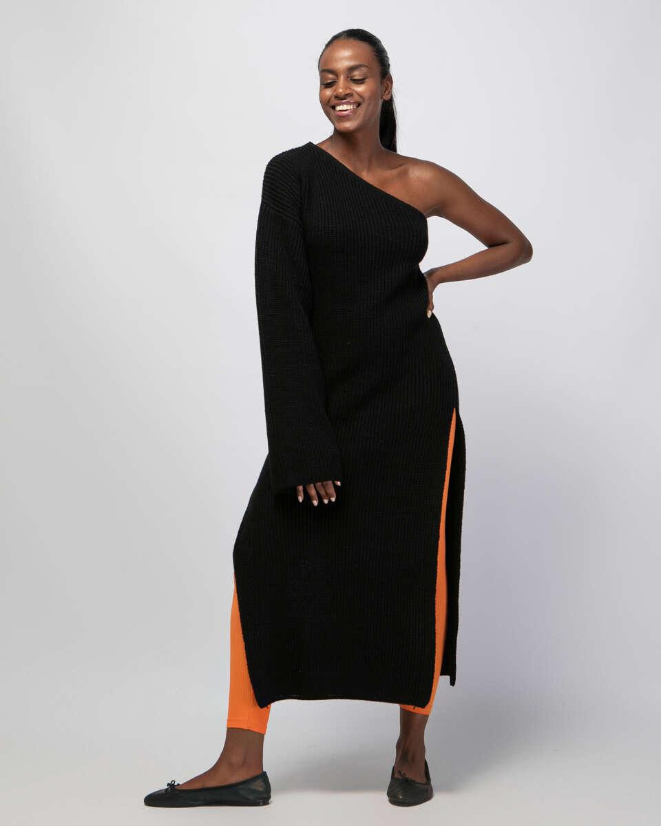 Μακριά μαύρη πλεκτή μπλούζα με έναν ώμο, φαρδύ μανίκι και ανοίγματα στα πλαϊνά. Εμφάνιση από μπροστά